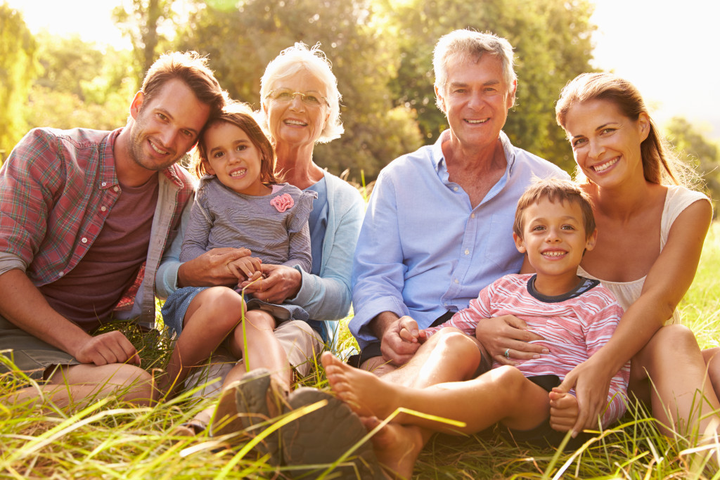 An extended family with children and grandparents, smiling to the camera while sitting on a grassy field