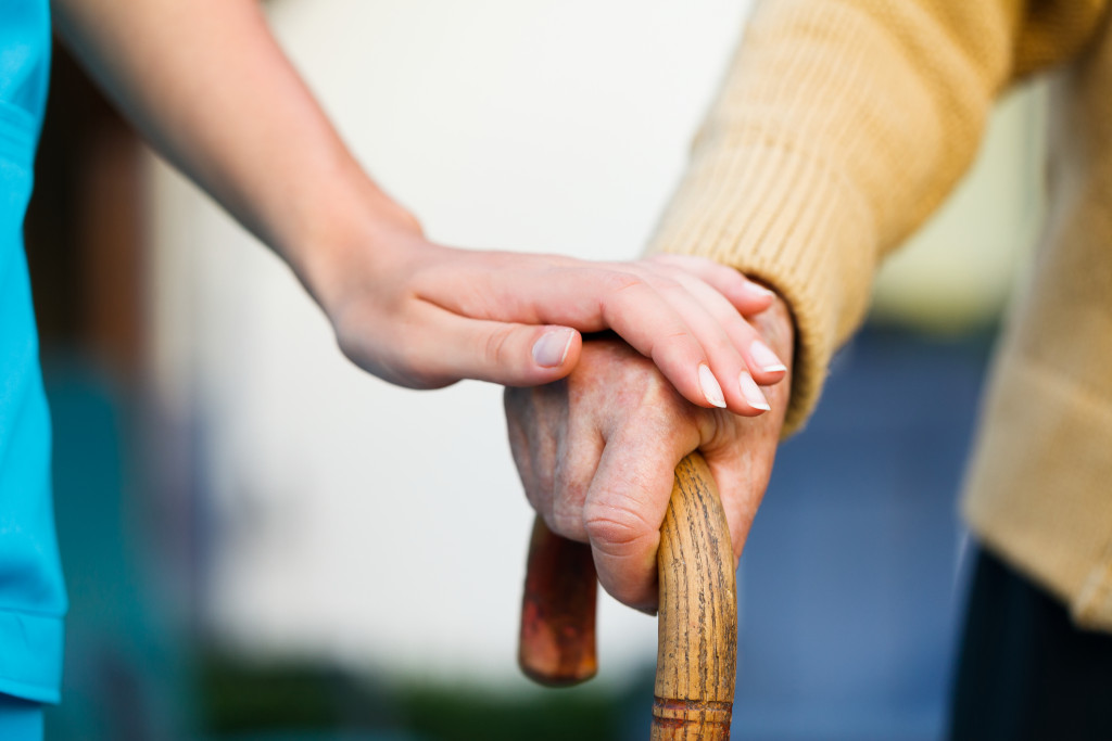 A caregiver holding the hands of a senior holding a cane