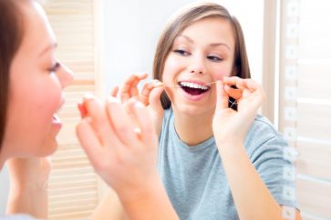 teenage girl flossing in mirror in bathroom