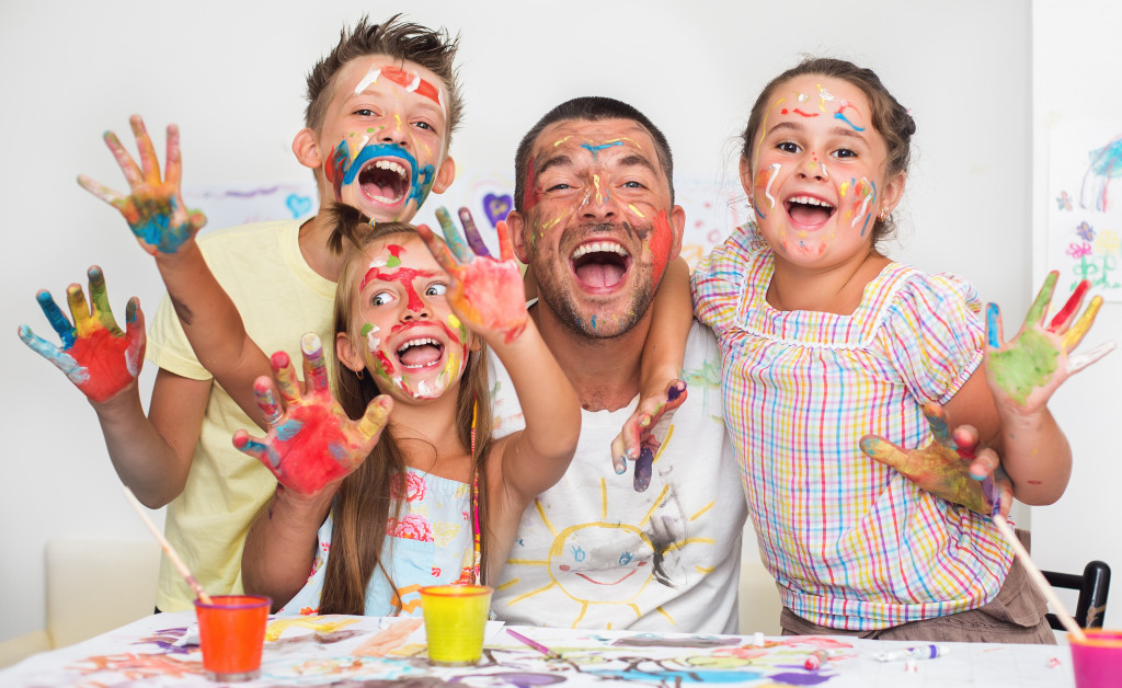 Father and three kids give happy smiles while their faces are covered in paint.