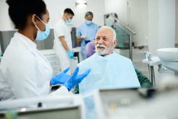 Black female dentist communicating with mature man during teeth exam at dentist's office