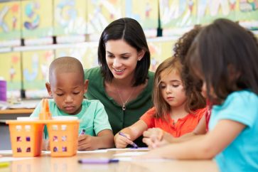 a female teacher teaching kids to draw using crayons in a table