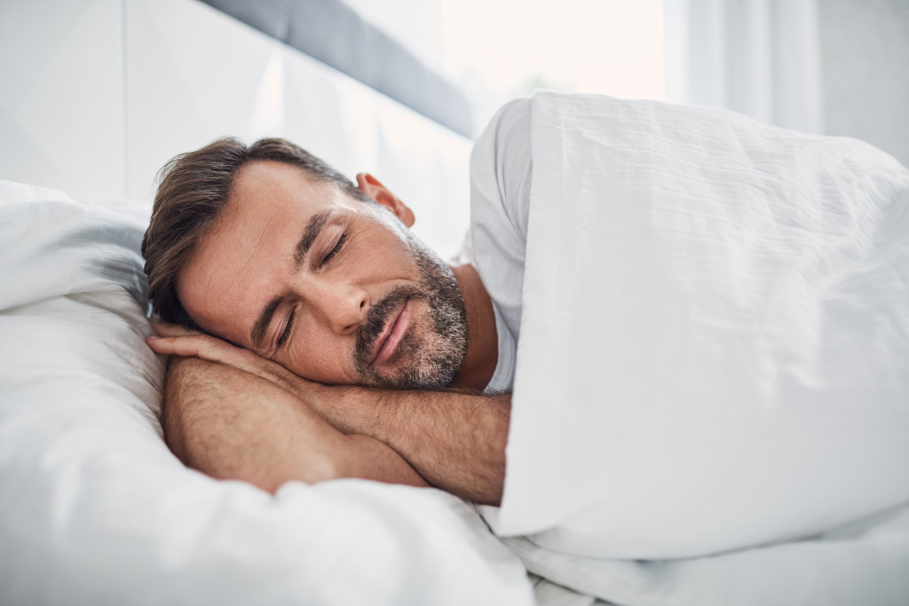 adult man asleep in bed in white sheets