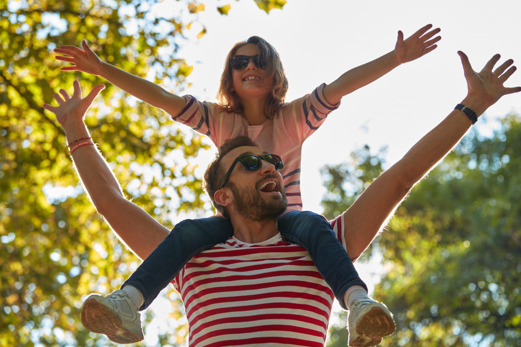 happy father outdoors with sunglasses and daughter in his shoulders
