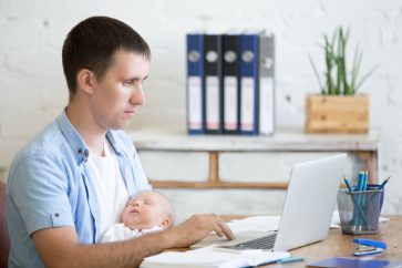 a father holding his baby while working